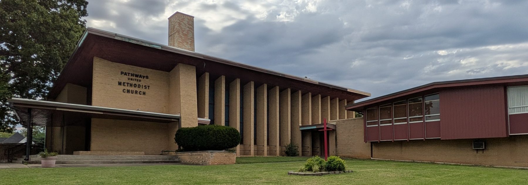 Pathways United Methodist Church, a tan brick building with tall columns and a red cross in the front lawn